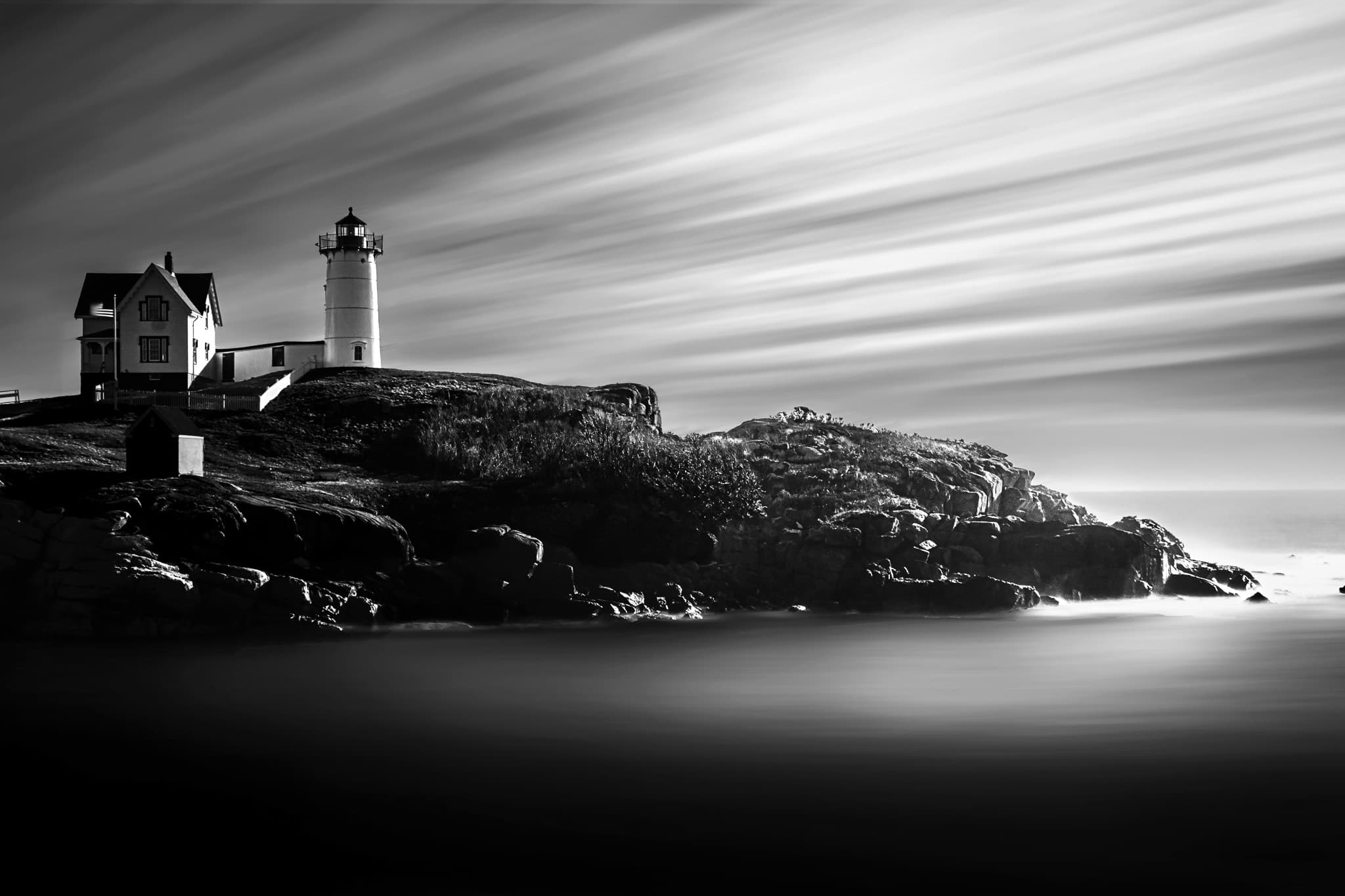 A white lighthouse and keeper's house on a rocky headland, the sky and sea smoothed to silk by a long exposure.