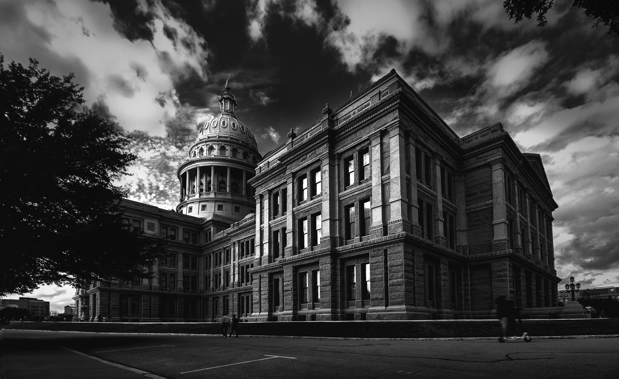 A grand domed neoclassical capitol building under a dramatic, cloud-streaked sky, seen from a low corner angle.